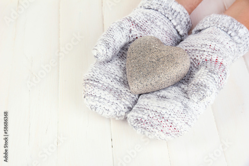 Female hands in mittens with heart on wooden background