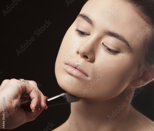 Beautiful woman applying makeup with a brush