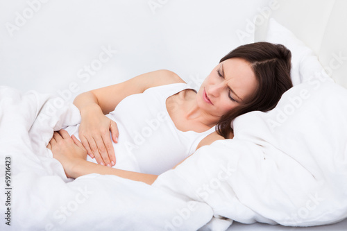 Woman with stomach ache lying on bed