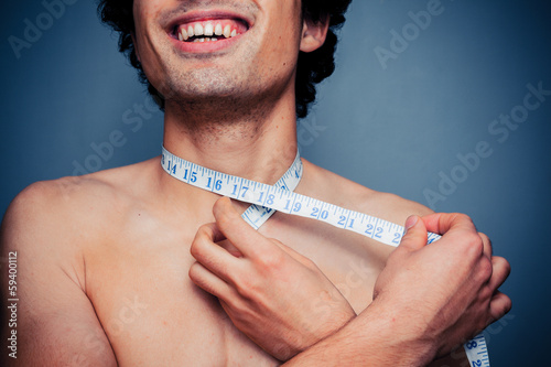 Happy young man is measuring his neck