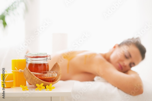 Closeup on honey spa therapy ingredients and woman in background