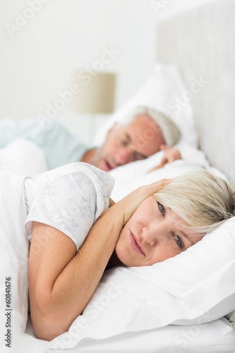 Woman covering ears while man snoring in bed