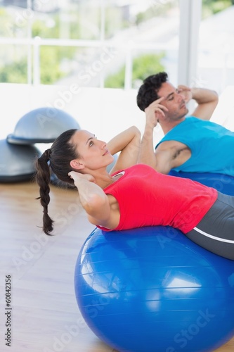 Fit couple exercising on fitness balls at gym