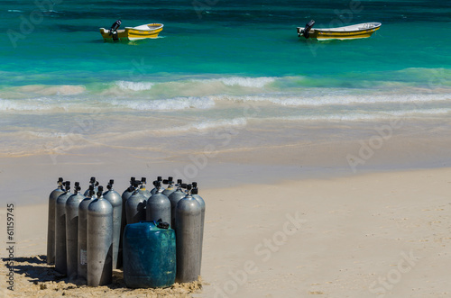 Scuba diving air tanks on sandy Caribbean beach with boats