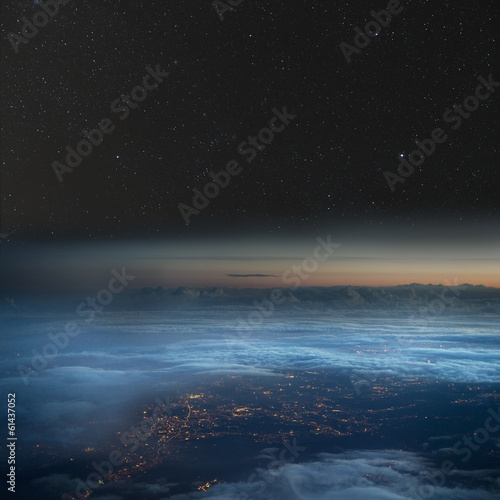 The Earth at night. City lights below the clouds, stars above.