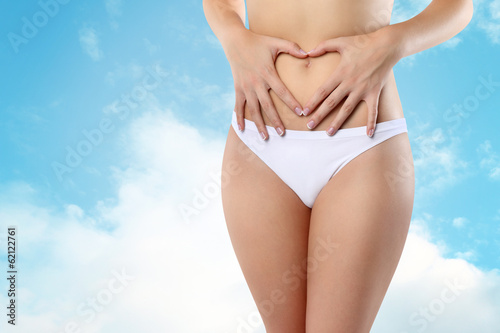 Woman's hands on stomach on sky background wellness concept