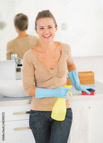 Portrait of happy housewife with spray bottle and sponge in bath