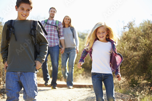 Mother And Children Hiking In Countryside Wearing Backpacks