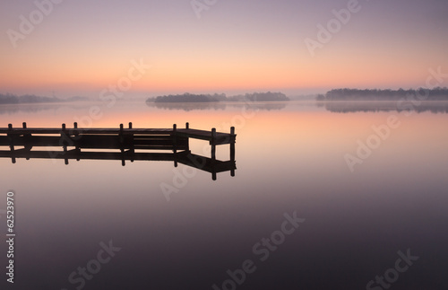 Jetty during a tranquil, foggy dawn at a lake.