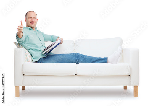 smiling man lying on sofa with book