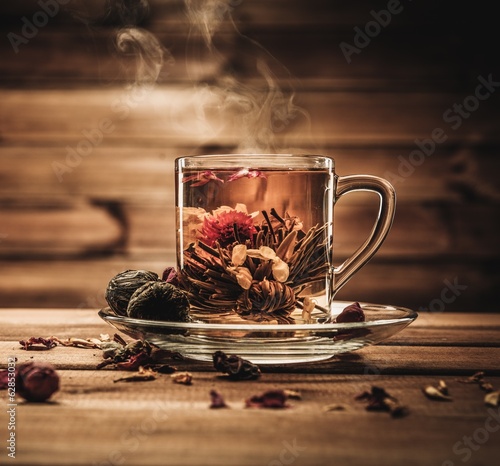 Glass cup with tea flower against wooden background