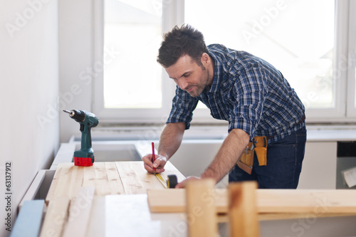 Smiling carpenter measuring wooden planks