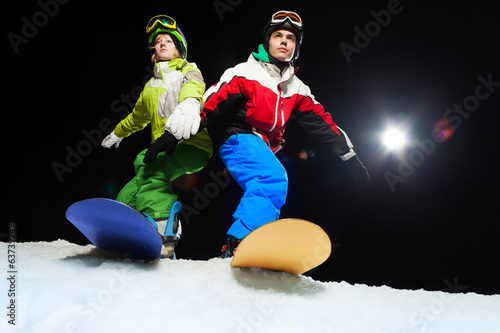 Two snowboarders ready to slide at night