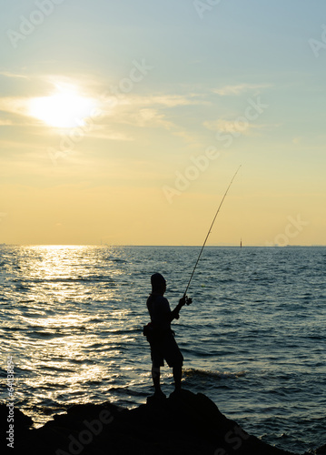 a man is fishing in evening and gold sunset background