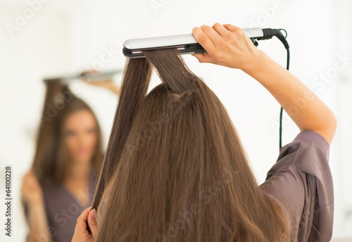 Young woman using hair straightener in bathroom. rear view