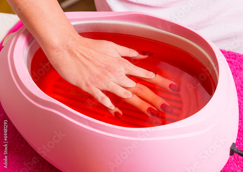 Female hand and orange paraffin wax in bowl. 