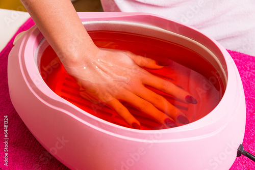 Female hand and orange paraffin wax in bowl. 