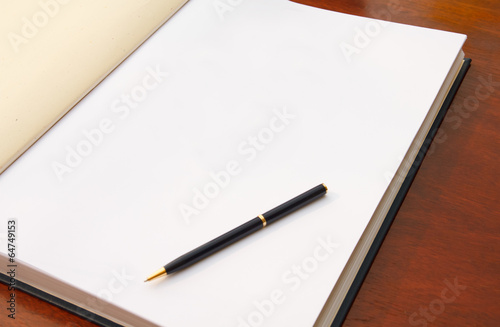 Large open book on wood table with white blank page and pen.