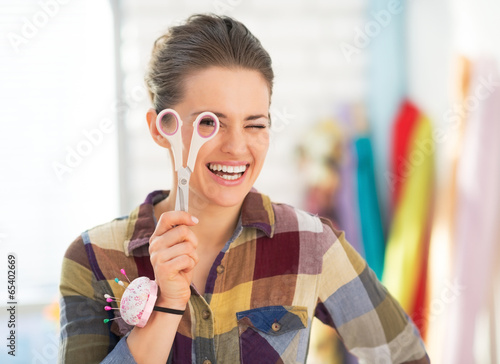 Smiling seamstress using looking through scissors