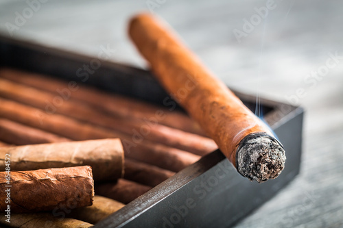 Burning cigar with smoke on wooden humidor