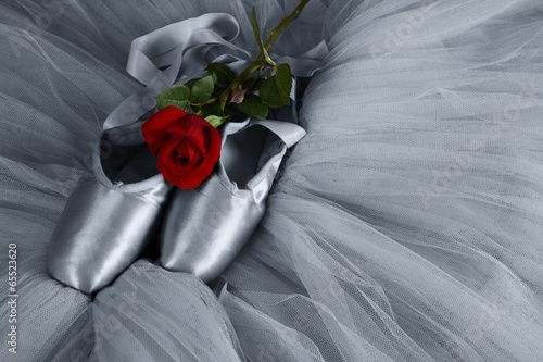 Old used ballet slippers lying on floor with rose and tutu artis