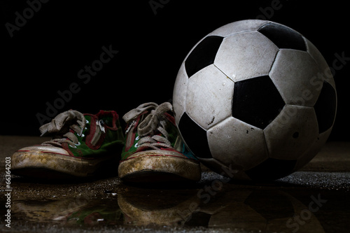 Dirty sneakers with soccer ball on black background