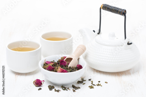 green tea with rosebuds, cups and teapot on white wooden table