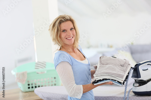 Smiling young housekeeper woman holding pile of clothes