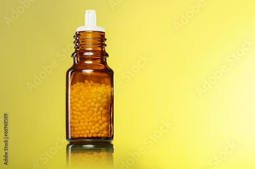 single bottle with homeopathy globules with yellow background