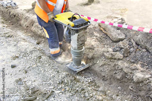 Worker uses compactor to firm soil at worksite