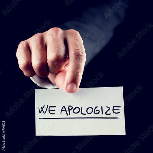 Businessman holding a card reading We Apologise