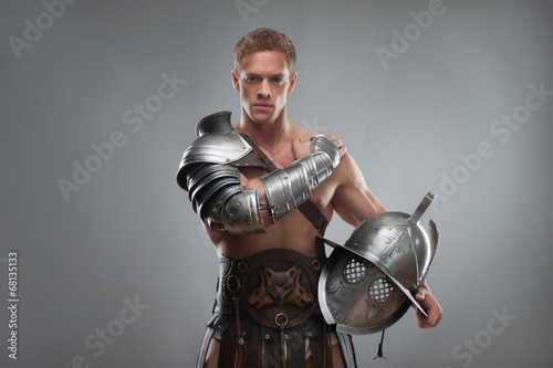 Gladiator in armour posing with helmet over grey background