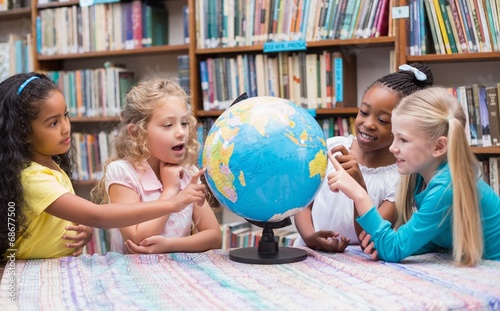 Cute mixed race pupils looking at globe in library