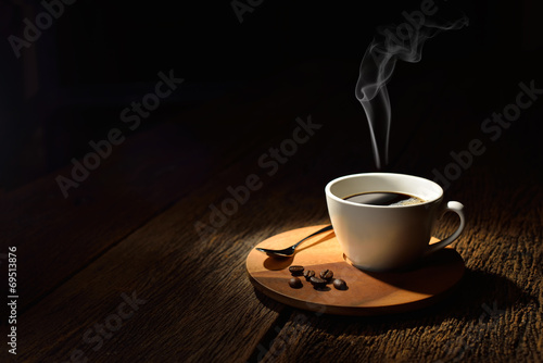 Cup of coffee with smoke and coffee beans on wooden background