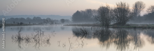 Panorama landscape of lake in mist with sun glow at sunrise