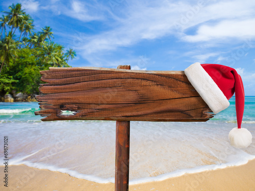 Christmas on beach concept. Wooden signboard with Santa's hat.