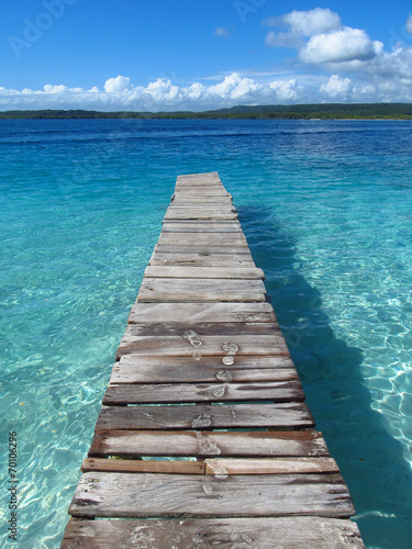 Huellas sobre un puente de madera en una playa cristalina