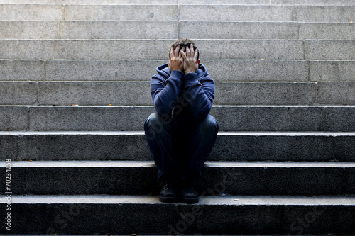 Young homeless man sad crying in depression on ground street