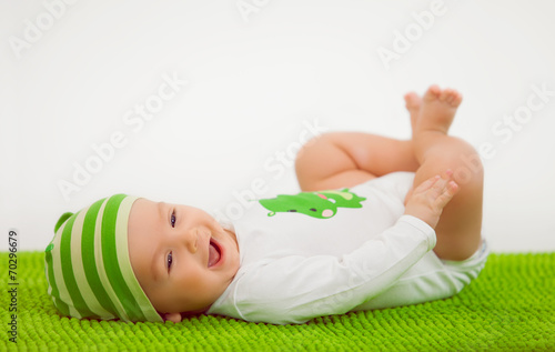 Smiling baby in a hat lying on the green soft carpet