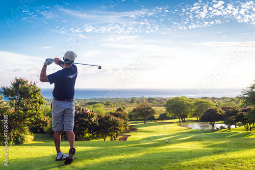 Man hitting golf ball down hill towards ocean and horizon