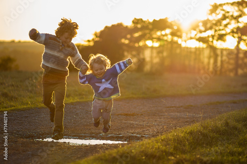 two boys jumping over puddles