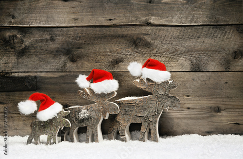 Three mooses wearing santa hats on grey wooden background