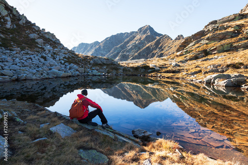 Male hiker takes a rest sitting next a mountain lake