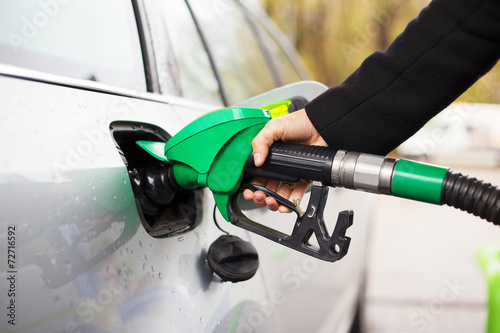 Hand holding fuel pump and refilling car at petrol station