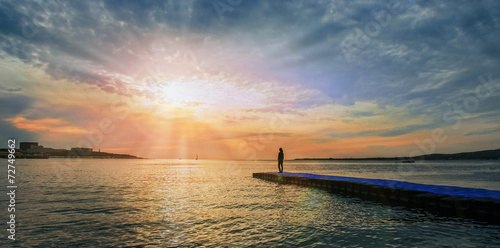 Woman standing on pier near the sea at sunset