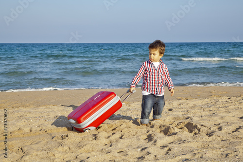 Niño pequeño arrastrando maleta por la arena de la playa