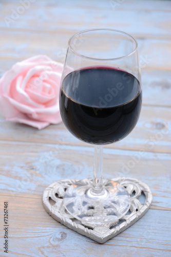 glas rode wijn op houten tafel met hart decoratie en roze roosje
