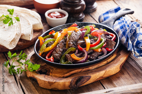 Beef Fajitas with colorful bell peppers in pan and tortilla brea