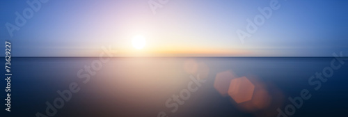 Conceptual image of sunset with added lens flare over still wate