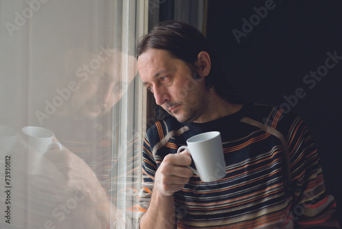 Sad man by the window drinking coffee